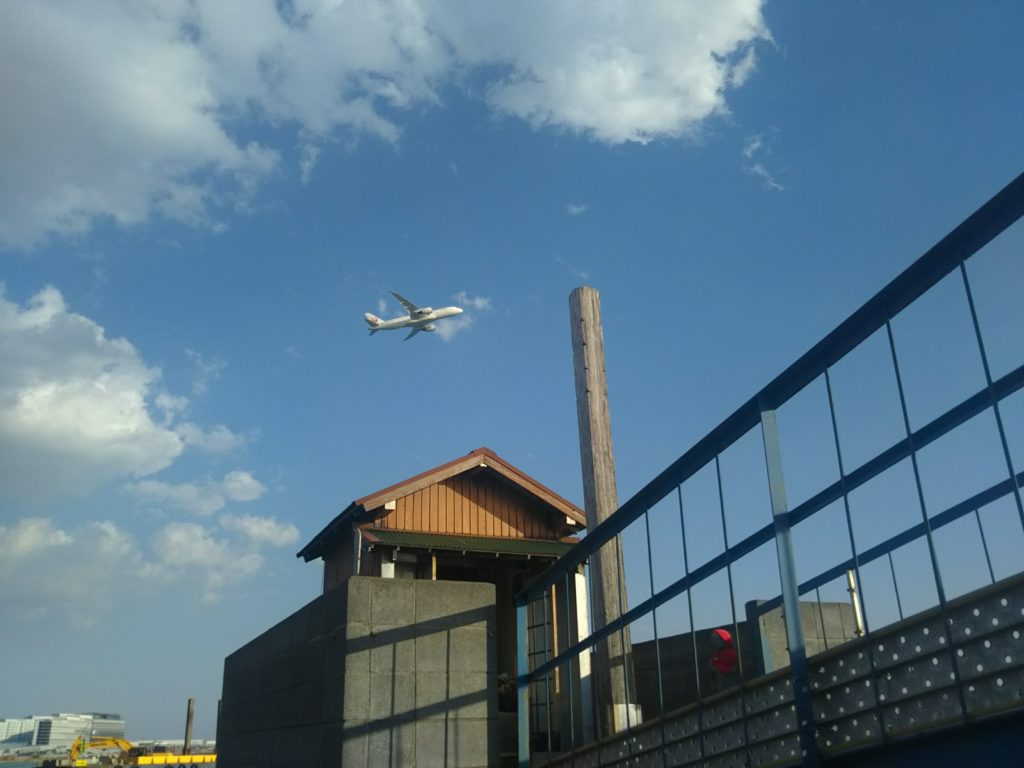 大田区羽田の五十間鼻無縁仏堂の上を新飛行ルートの飛行機が飛んでいきます。
